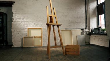 Bir sanat stüdyosunda, bir kutunun yanında tuvallerin arka planına karşı bir tripod vardır.