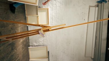 Bir sanatçının bir sanat stüdyosunda çekilen dikey video, beyaz tuvali üç ayaklı bir banda yerleştirir.