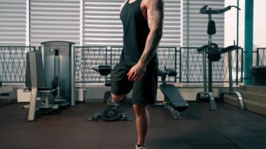 Spor salonunda siyah tişörtlü yakışıklı adam egzersiz makinesinin önünde ısınma egzersizi yapıyor.