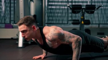 Spor salonunda siyah tişörtlü yakışıklı bir adam yerde şınav çekiyor.
