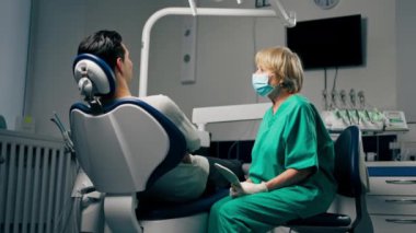 Bir dişçi kliniğinde, elinde ayna tutan ve konsültasyon yapan bir kadın diş hekimi olan bir hasta.