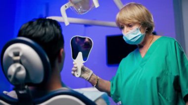 Bir dişçi kliniğinde ayakta duran bir dişçi, aynanın karşısında hastayla ilgili bir sorunun varlığını gösterir.