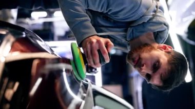 Dikey video. Bir benzin istasyonunda araba tamircisi son cilalamayı yapıyor.