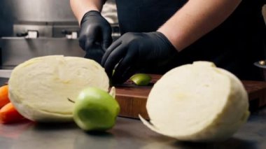Profesyonel bir mutfakta, siyah eldivenler giyerek, tahta üzerinde yeşil bir elma keserek.