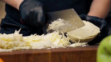 Profesyonel bir mutfakta, siyah eldivenler giyerek, tahta tahtada lahana keserek.