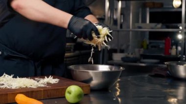 Profesyonel bir mutfağa yakın plan siyah eldivenler giyip demir bir kaseye lahana döker.