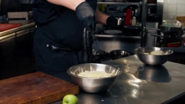 Profesyonel bir mutfakta siyah eldivenler giyip demir bir kasede lahana tuzluyorlar.