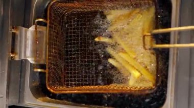 Profesyonel bir mutfakta yakın plan çekilen dikey video fritözde yağda patates kızartması.