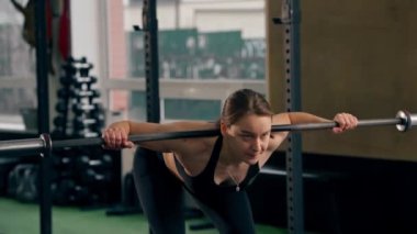 Spor salonunda siyah bluzlu bir kız antrenör halterle egzersiz yapıyor.