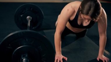 Spor salonunda bir kız antrenör halterle çalıştıktan sonra yerde zıplar ve uzanır.