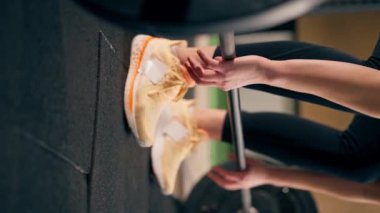 Spor salonundaki dikey çekimde siyah taytlı bir kız antrenör ağırlığıyla halteri kaldıracak.