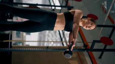 Spor salonundaki dikey video siyah taytlı bir kız antrenör ve bir top ağırlık ile çalışıyor.