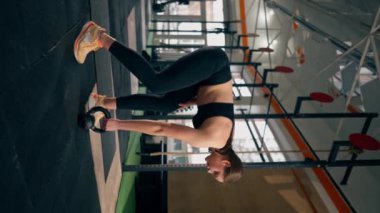 Spor salonundaki dikey video siyah taytlı bir kız antrenör ve bir top ağırlık ile çalışıyor.