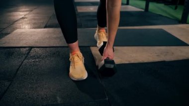 Spor salonunda bir kız antrenör bir eliyle dambılı kaldırıyor ve gülümsüyor.