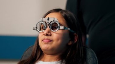 Optalmoloji kliniğinde obez bir doktor, bir kızın lens seçmesi için geçici gözlük dener.