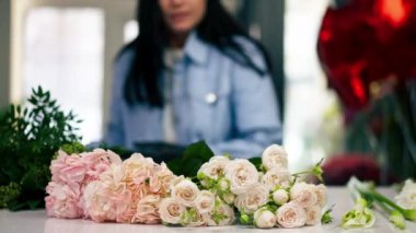 Çiçekçi bir kız beyaz bir masanın yanında güzel bir buket beyaz çiçek topluyor.