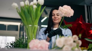 Çiçekçi bir kız beyaz bir masanın yanında güzel bir buket beyaz çiçek topluyor.