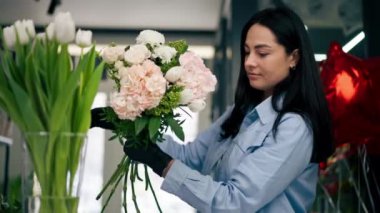 Çiçekçi bir kız beyaz bir masanın yanında güzel bir buket beyaz çiçek topluyor.