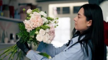 Çiçekçiyi kapatın. Beyaz bir masanın yanında bir kız çiçek demeti dolusu beyaz çiçek topluyor.