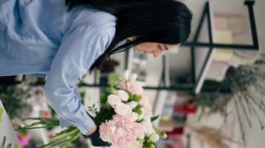 dikey video çiçek dükkanı beyaz masaya yakın bir kız güzel bir buket beyaz çiçek topluyor.