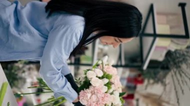 dikey video çiçek dükkanı beyaz masaya yakın bir kız güzel bir buket beyaz çiçek topluyor.
