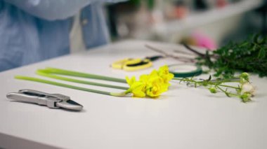 Beyaz bir masanın üzerindeki çiçekçi dükkanında bir buket çiçek hazırlamak için çiçekçi malzemeleri var.