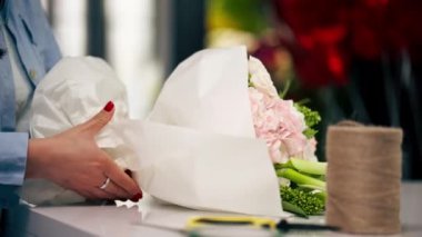 Çiçekçide bir çiçekçi hazır narin bir buketi beyaz bir kağıda sarar.