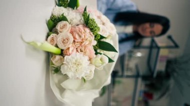 Çiçekçide dikey bir video. Çiçekçi hazır narin bir buketi beyaz bir kağıda sarar.