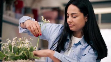 Bir çiçekçiye yakın bir yerde beyaz bir masaya yakın bir kız çiçek toplar sepetinde bir buket çiçek düzenler.