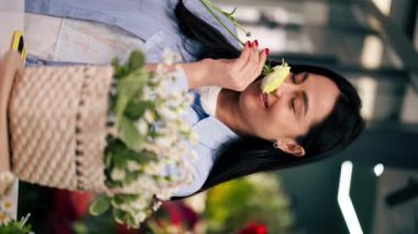 dikey video bir çiçekçide kapanır beyaz bir masanın yakınındaki bir kız bir çiçek aranjmanı toplar sepetteki bir buketi