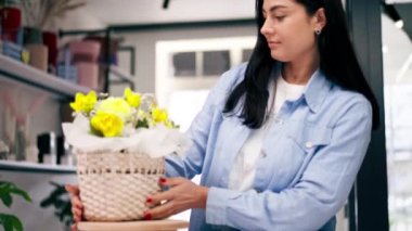 Bir çiçekçide bir çiçekçi, sepetteki sarı çiçeklerle tamamlanmış bir çiçek düzenine hayran kalır.