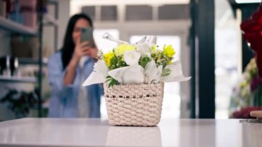 Çiçekçide bir çiçekçi telefonundaki sepetin içinde toplanmış sarı bir buketin fotoğrafını çeker.