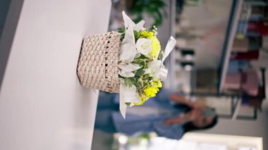 Çiçekçi dükkanındaki dikey videoda çiçekçi telefonundaki sepetin içinde toplanmış sarı bir buketin fotoğrafını çekiyor.