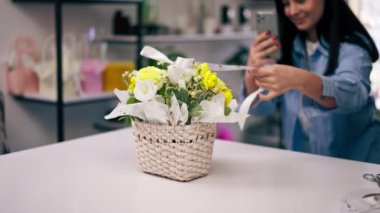 Çiçekçide bir çiçekçi telefonundaki sepetin içinde toplanmış sarı bir buketin fotoğrafını çeker.