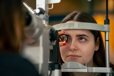 Bir göz hekimliği kliniğinde genç bir doktor büyüteçle genç bir kıza teşhis koyuyor.