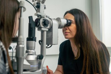 Bir göz hekimliği kliniğinde genç bir doktor büyüteçle genç bir kıza teşhis koyuyor.