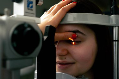 Bir göz hekimliği kliniğinde genç bir doktor büyüteçle genç bir kıza teşhis koyuyor.