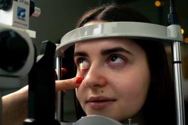 Bir göz hekimliği kliniğinde genç bir doktor büyüteçle genç bir kıza teşhis koyuyor.