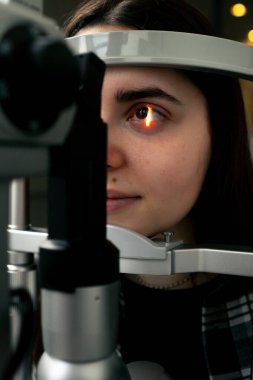 Bir göz hekimliği kliniğinde genç bir doktor büyüteçle genç bir kıza teşhis koyuyor.