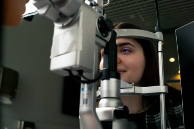 Bir göz hekimliği kliniğinde genç bir doktor büyüteçle genç bir kıza teşhis koyuyor.