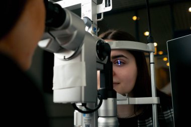 Bir göz hekimliği kliniğinde genç bir doktor büyüteçle genç bir kıza teşhis koyuyor.