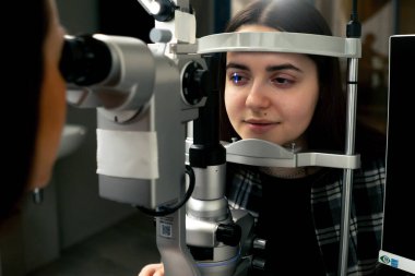 Bir göz hekimliği kliniğinde genç bir doktor büyüteçle genç bir kıza teşhis koyuyor.