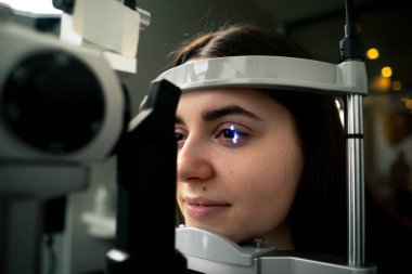 Bir göz hekimliği kliniğinde genç bir doktor büyüteçle genç bir kıza teşhis koyuyor.