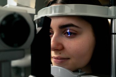 Bir göz hekimliği kliniğinde genç bir doktor büyüteçle genç bir kıza teşhis koyuyor.