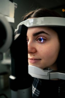 Bir göz hekimliği kliniğinde genç bir doktor büyüteçle genç bir kıza teşhis koyuyor.