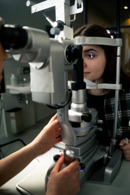 Bir göz hekiminde genç bir doktor büyüteçle genç bir kıza teşhis koyuyor.