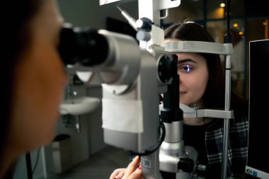 Bir göz hekiminde genç bir doktor büyüteçle genç bir kıza teşhis koyuyor.