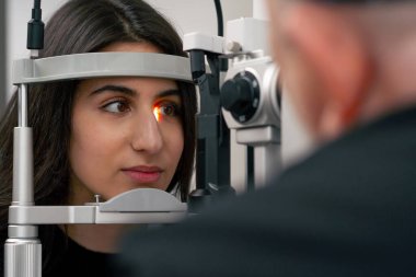 Göz hekimliği kliniğinde yaşlı bir doktor büyüteçle genç bir kıza teşhis koyuyor.
