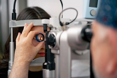 Göz hekimliği kliniğinde yaşlı bir doktor büyüteçle genç bir kıza teşhis koyuyor.