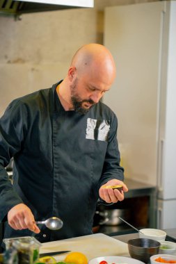 Profesyonel bir mutfakta siyah ceketli bir şef avokadoyu somonlu tost için hazırlar.